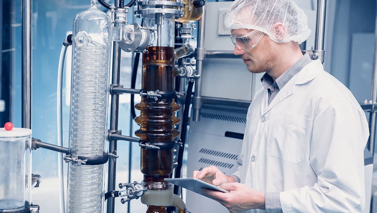 a man in a white coat and goggles looking at a device