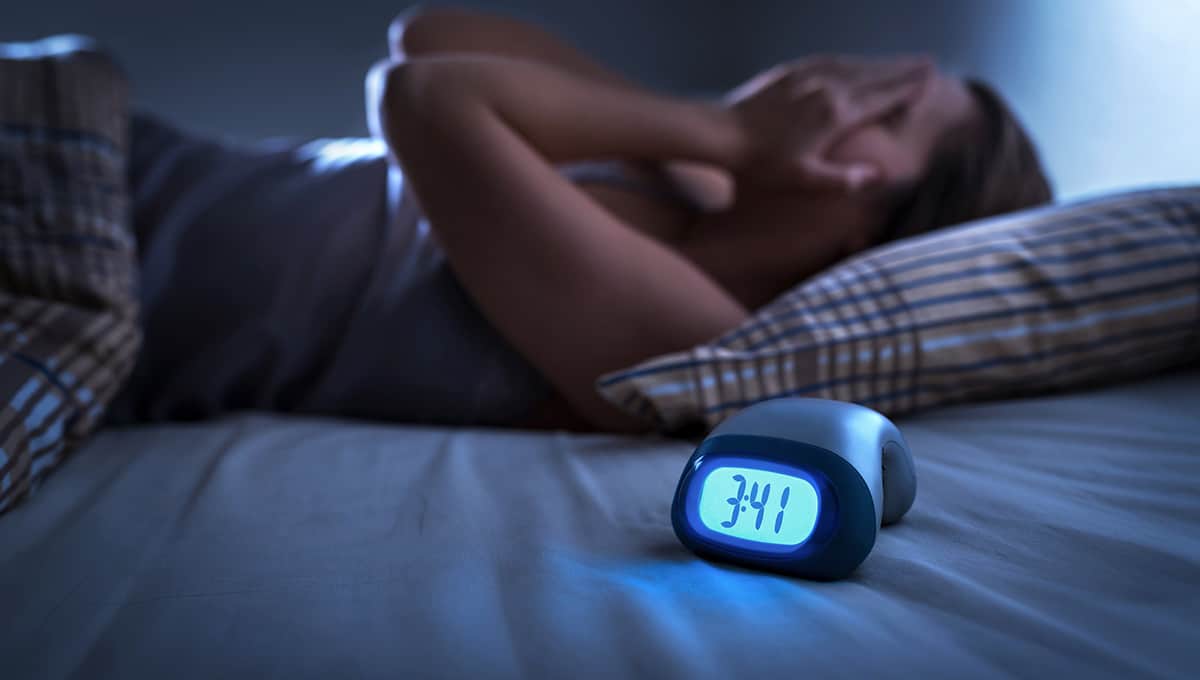 a woman lying in bed with a digital clock